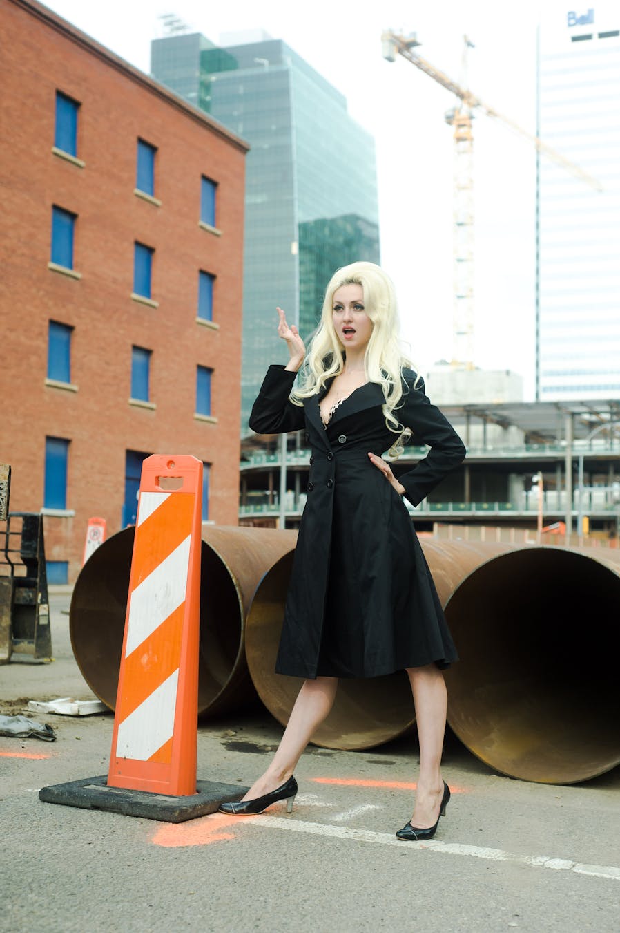 A stylish woman poses confidently in a black dress amidst urban construction, blending fashion with an industrial backdrop.