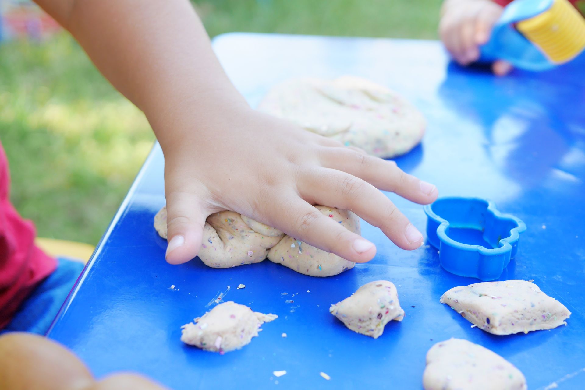 Young child having fun playing with colorful clay at an outdoor table.