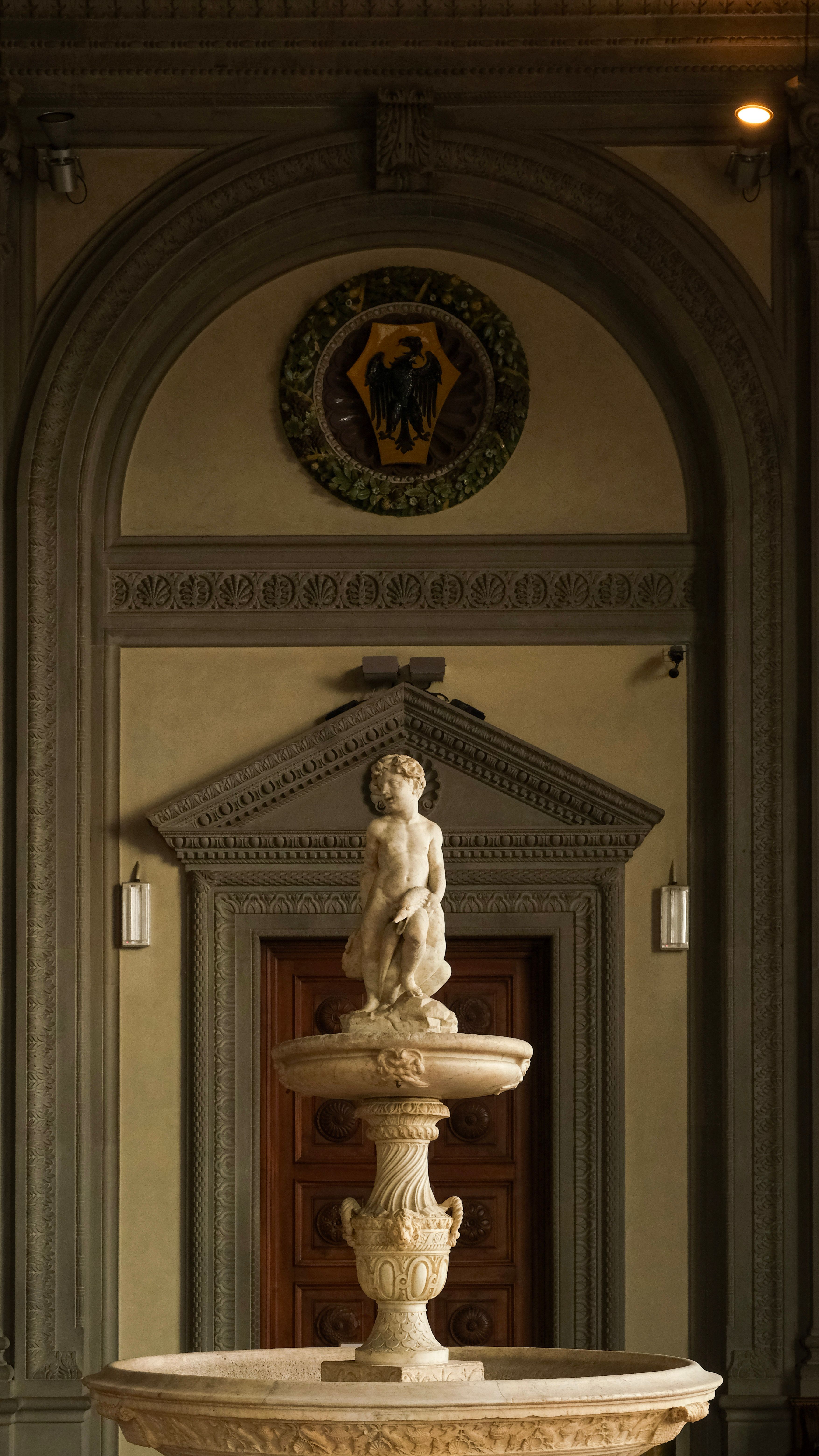 Vertical shot of a classical sculpture in an ornate museum interior with warm lighting.