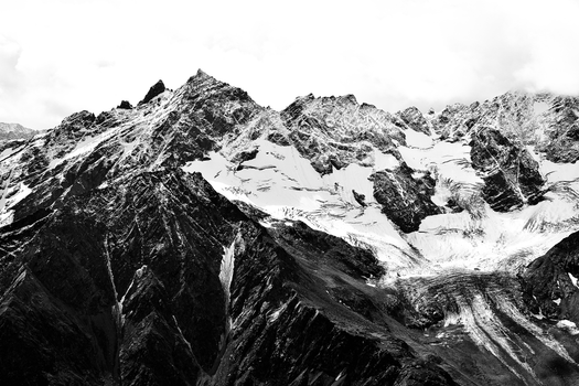 Black and white photo of snowcapped mountain peaks with rugged terrain.