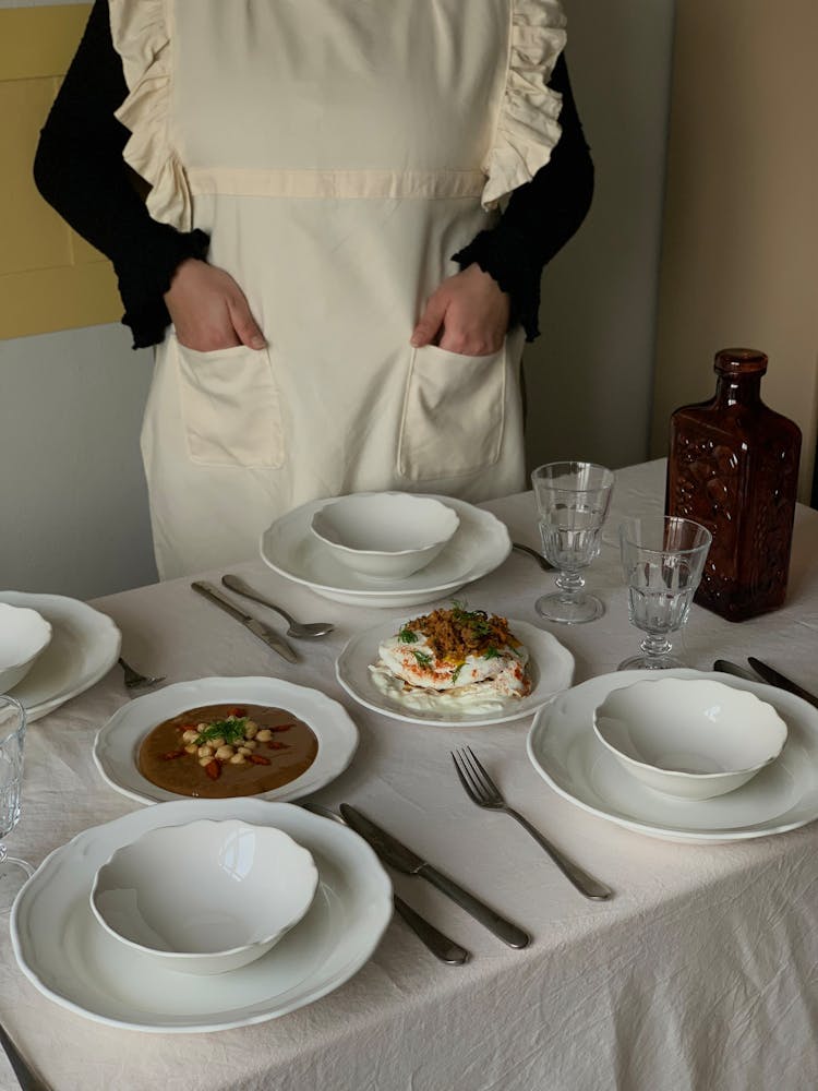 Woman In An Apron Standing Behind A Set Table 