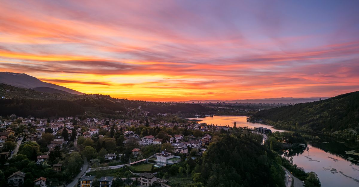 A breathtaking aerial view of Pancharevo, Sofia, Bulgaria, at sunset with vibrant colors over the hills and lake.