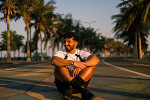 Young man sitting on a vibrant street in Jeddah surrounded by palms.