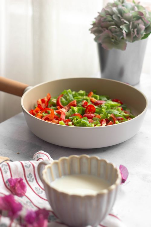 Free Colorful vegetables in a frying pan ready for cooking, framed by cozy kitchen decor. Stock Photo