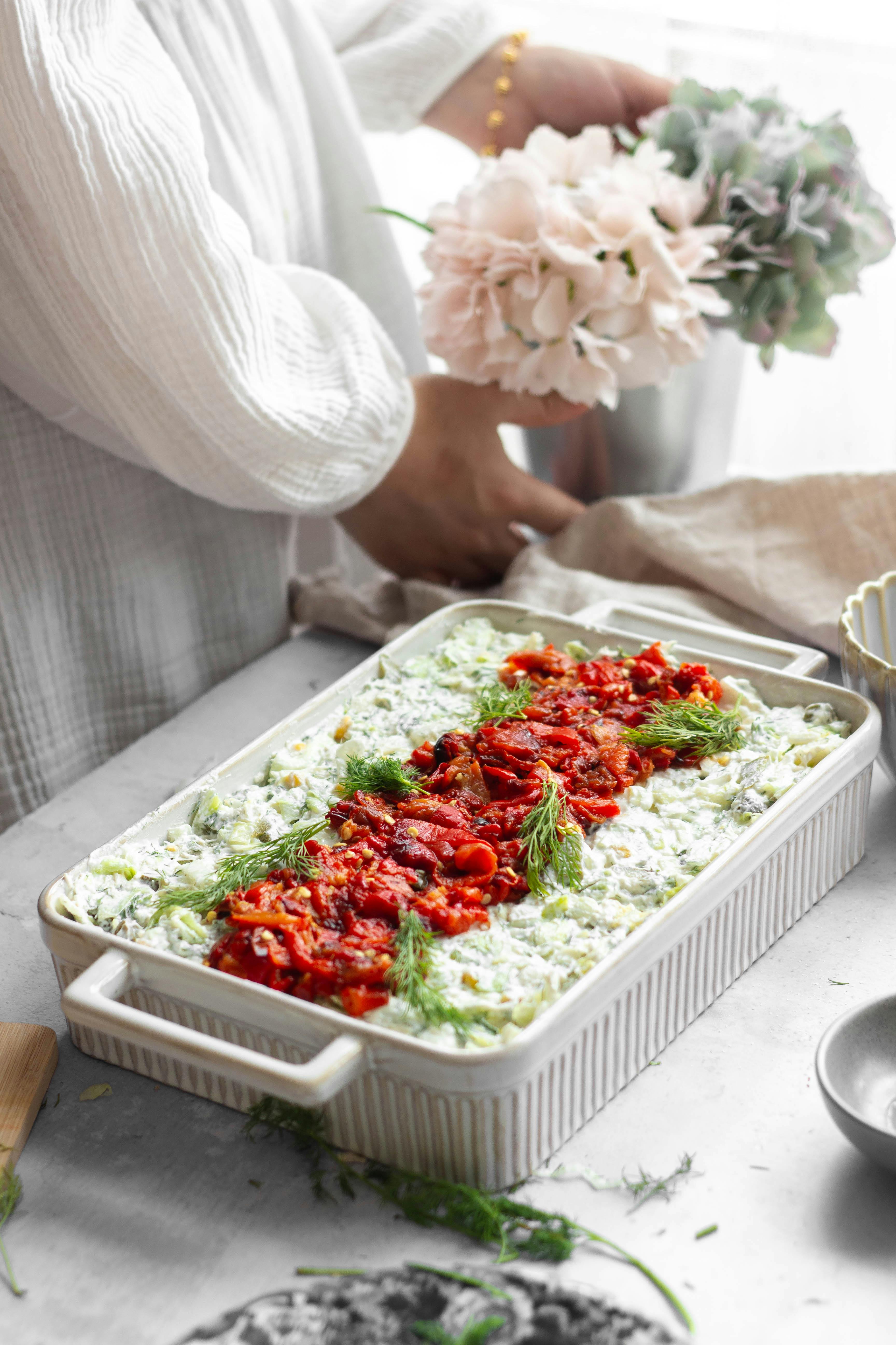 Hands arranging flowers next to a fresh vegetable casserole, highlighting healthy cooking.