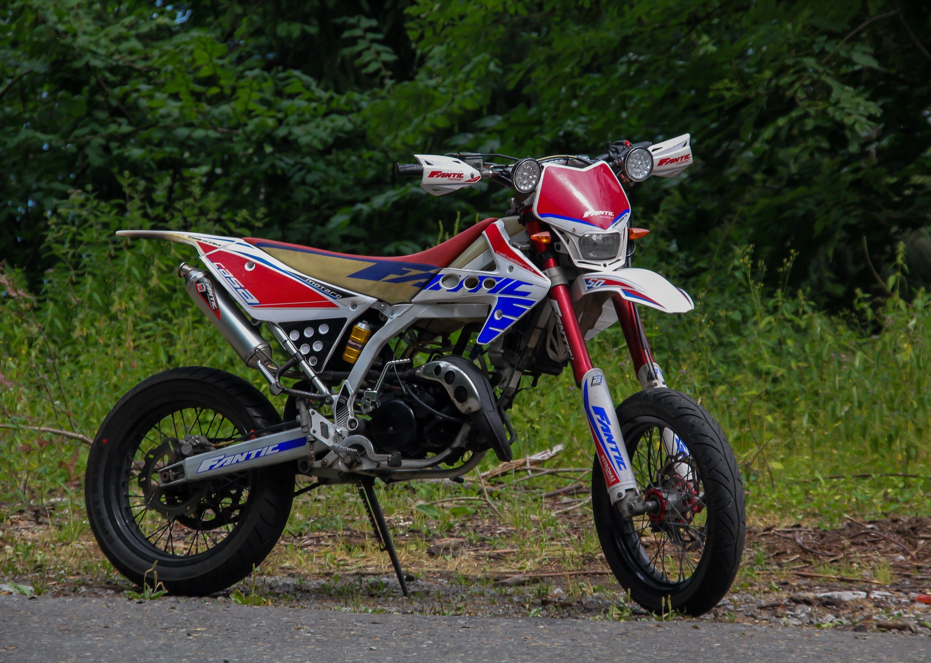An off-road dirt bike parked at the edge of a country road with greenery all around, a real stock photo with no people in the frame, chosen because Trials is the motorbike obstacle-course series made by the studio this story is about
