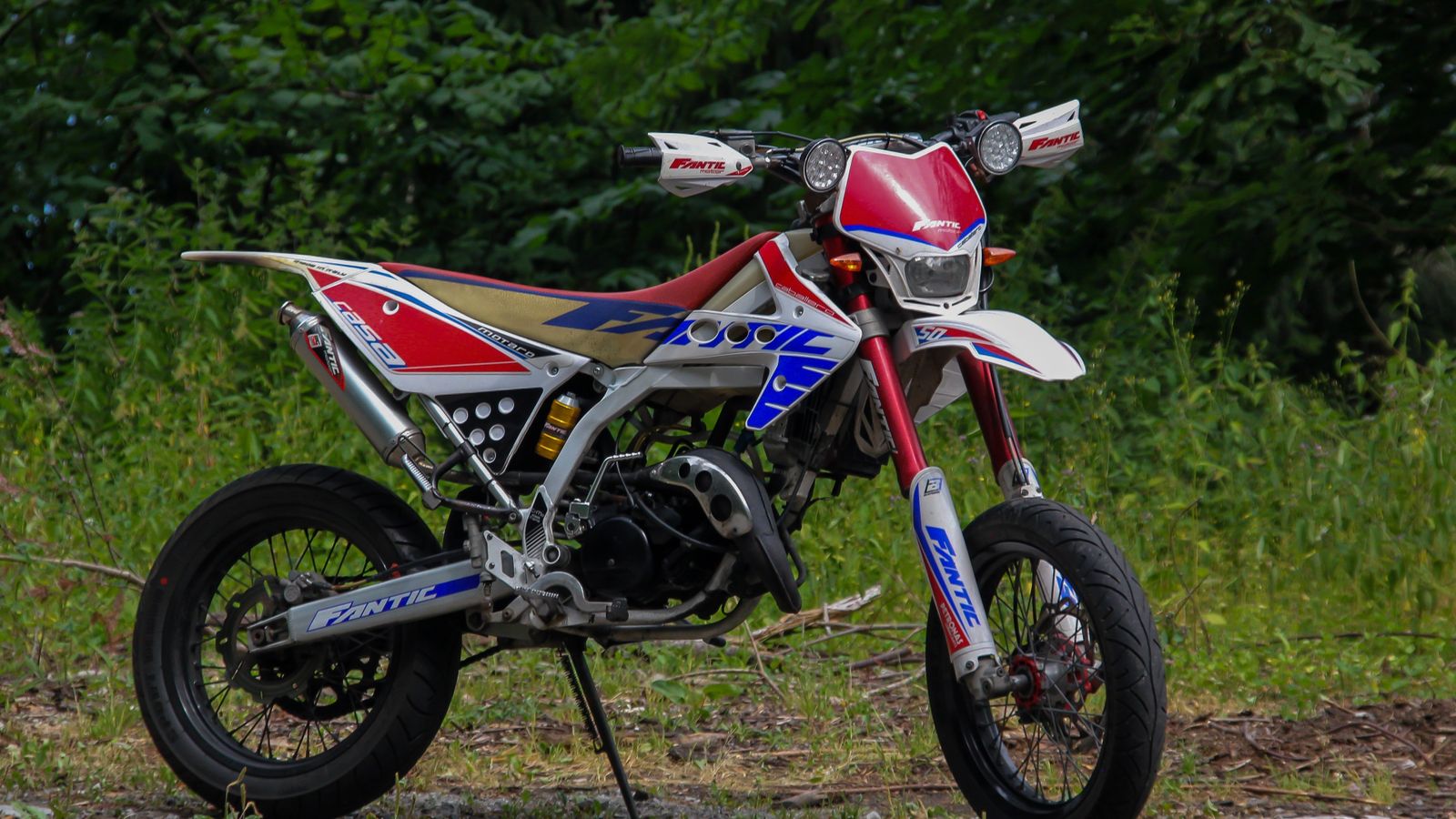 An off-road dirt bike parked at the edge of a country road with greenery all around, a real stock photo with no people in the frame, chosen because Trials is the motorbike obstacle-course series made by the studio this story is about