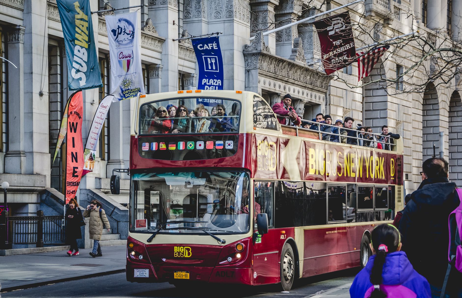 Double-decker bus with tourists sightseeing in downtown New York City on a sunny day.