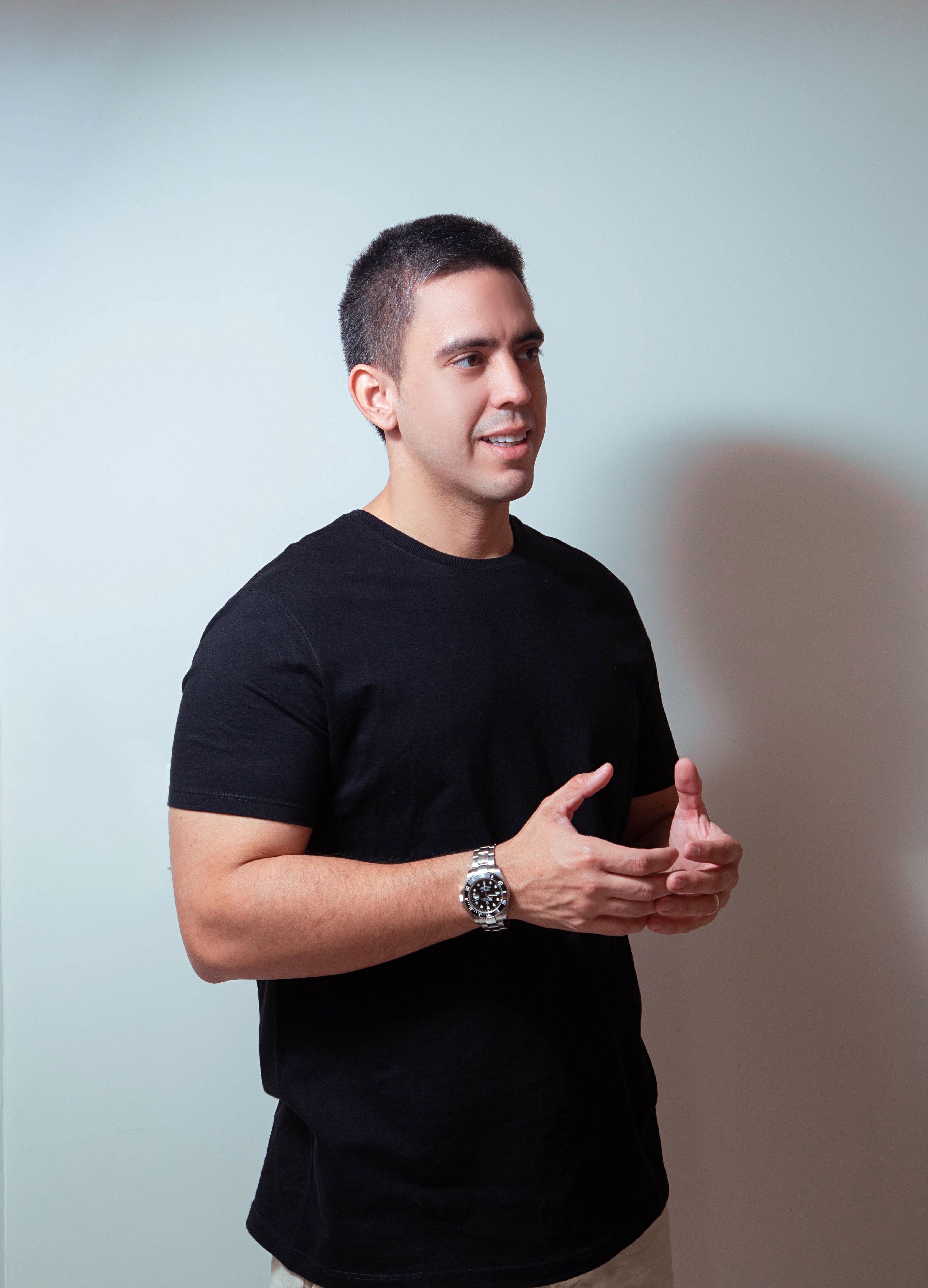 Smiling man wearing a black t-shirt gesturing in a studio with soft lighting.