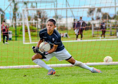 Young male goalkeeper in action making a soccer save during an outdoor match.