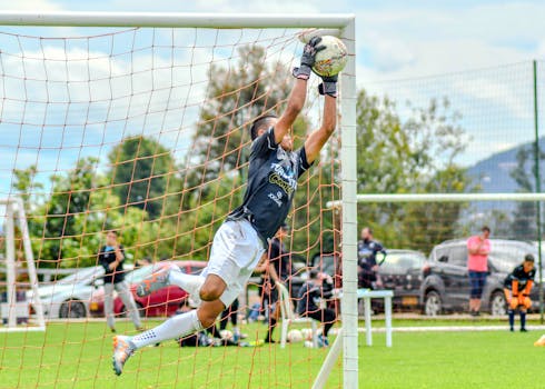 Goalkeeper leaping mid-air to catch the ball during a lively soccer match outdoors.