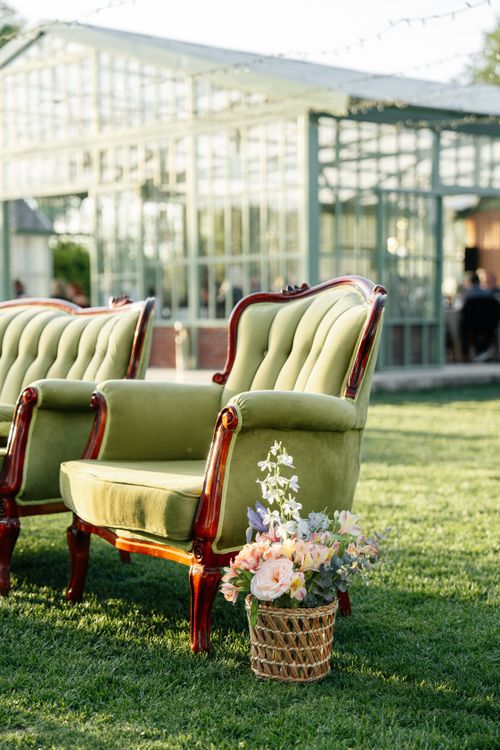 Free Vintage armchairs on green grass outside a greenhouse, adorned with a floral basket. Stock Photo