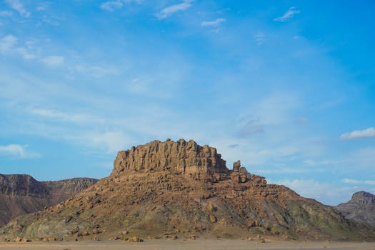 A majestic butte rises from the arid desert under a clear blue sky, showcasing rugged natural beauty.