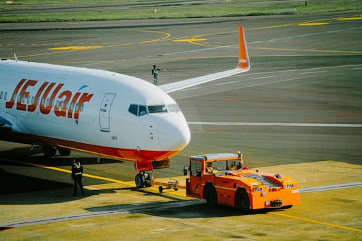 Commercial airplane being towed on airport tarmac by tug vehicle, ground crew working.