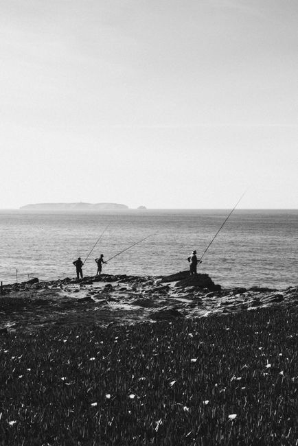 Three people fishing by the coast in black and white, showcasing a serene hobby.