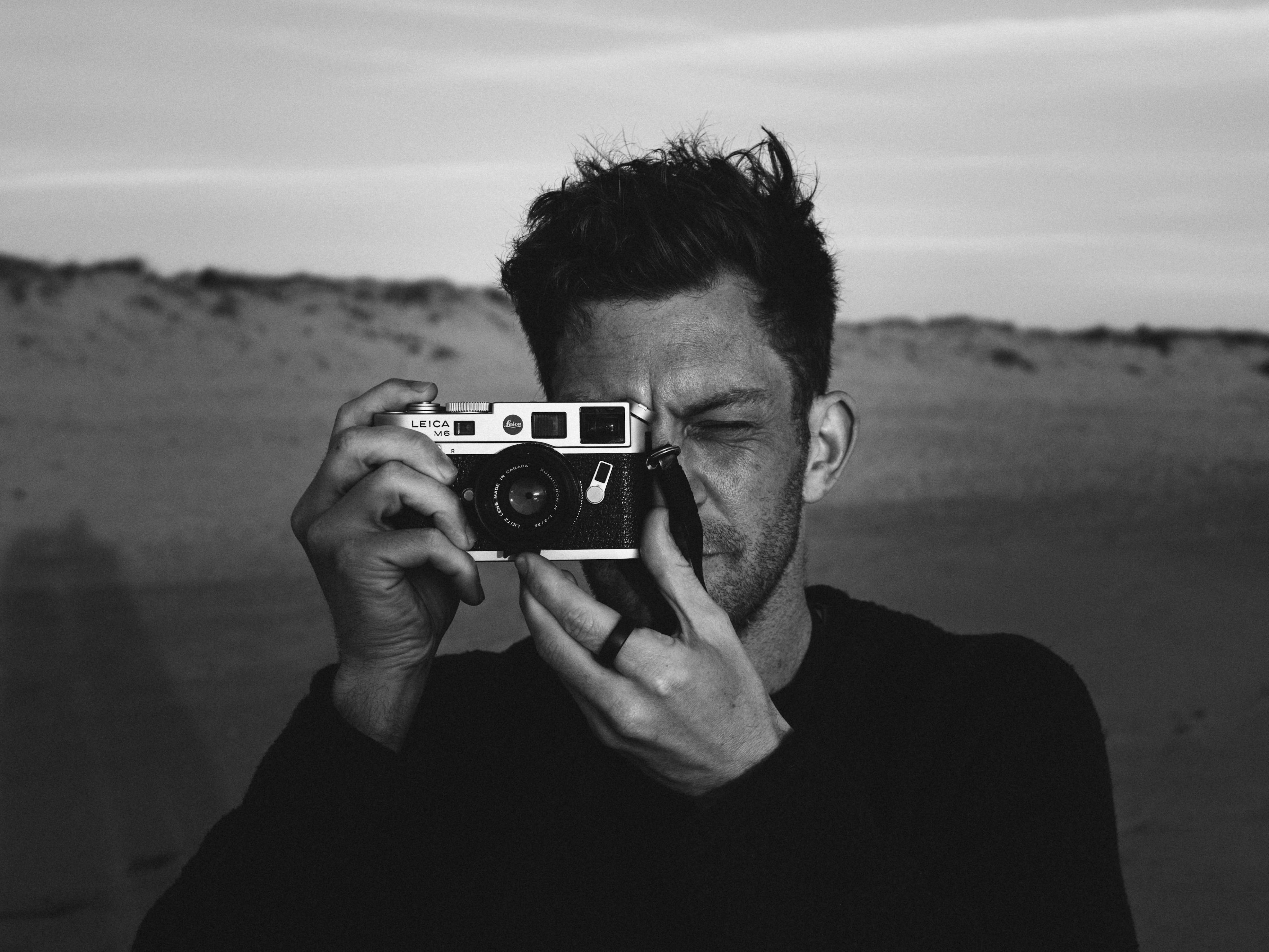 Captivating black and white portrait of a man using a vintage camera outdoors.