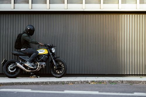 Free Man on yellow Ducati motorcycle against urban wall in London, wearing helmet and backpack. Stock Photo