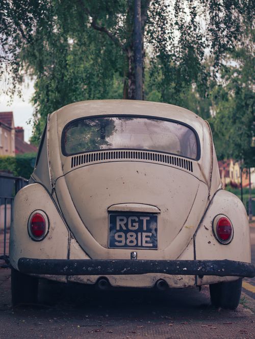Free Back view of a classic white Volkswagen Beetle parked on a London street with lush greenery. Stock Photo
