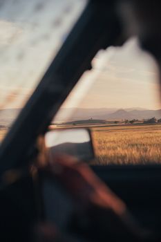Capturing a peaceful drive in a car through rural fields with mountains at sunset, perfect travel vibe.