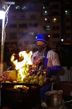 A street vendor grilling skewers in La Paz's vibrant night market, surrounded by flames and smoke.
