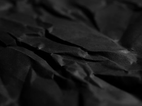 A close-up of crumpled black paper texture creating a dramatic abstract background.
