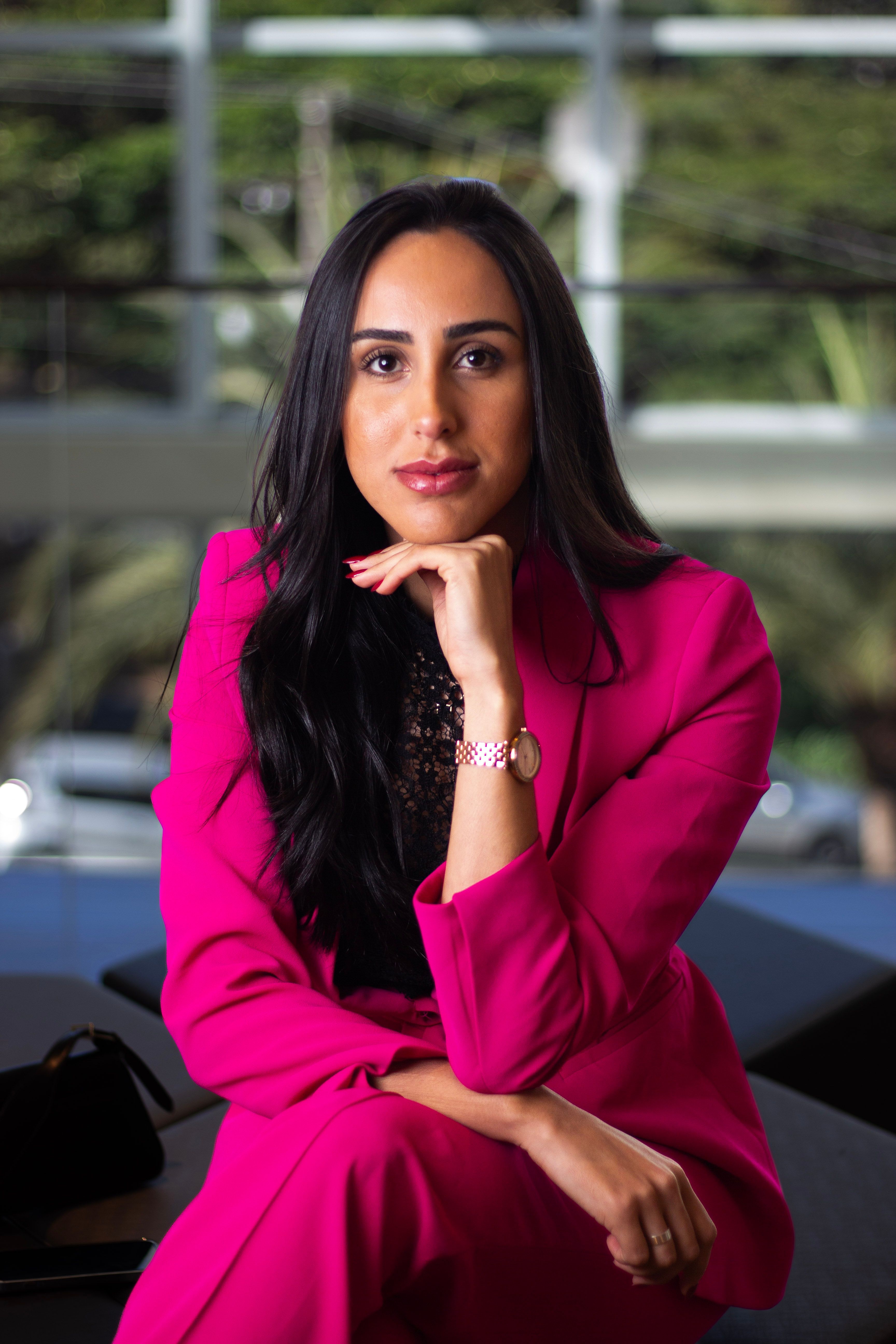 Portrait of a confident woman in a stylish pink suit, sitting indoors.