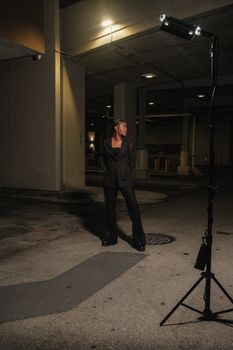 Portrait of a woman in a black jacket standing in an urban parking lot at night.