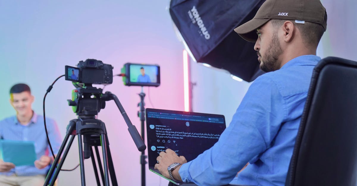 Man operates camera and laptop during a studio video shoot with a host and camera crew.