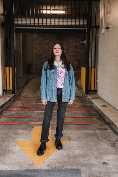 Young Woman in a Casual Outfit with a Jean Jacket Standing at the Entrance to a Garage 