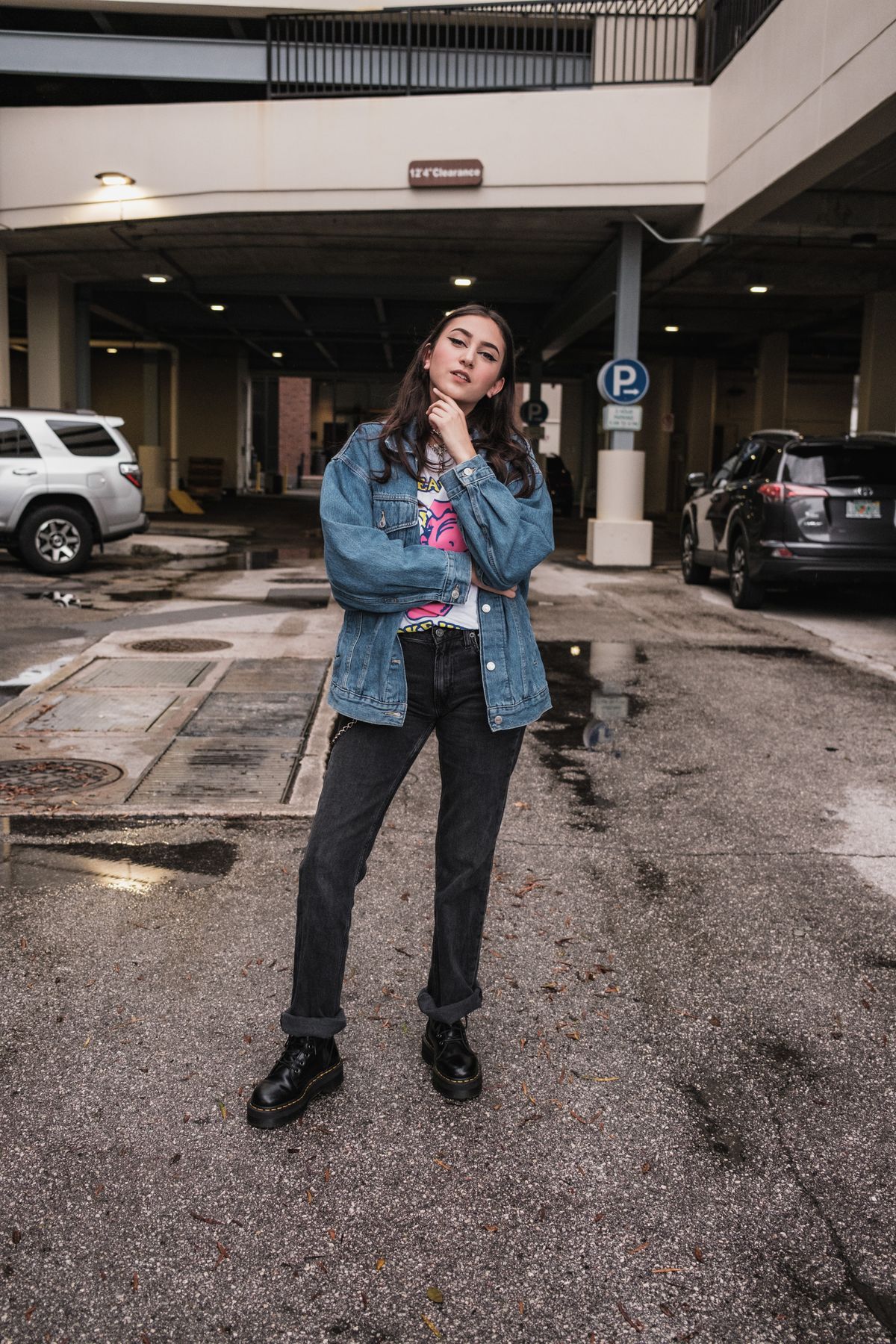A person in an oversized denim jacket and dark jeans standing in a parking garage