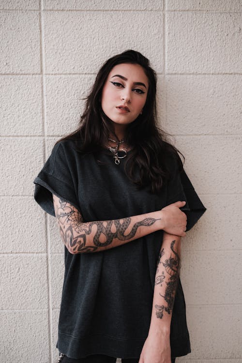 A woman with tattoos standing against a wall