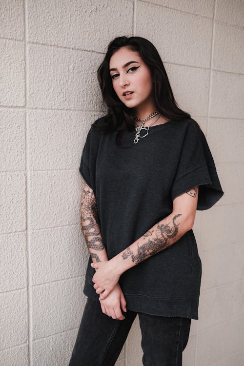 A woman with tattoos standing against a wall
