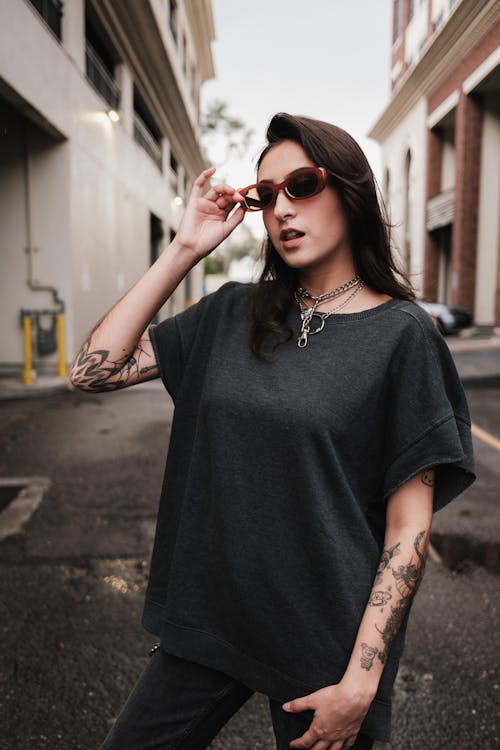 A woman with tattoos and sunglasses standing on the street