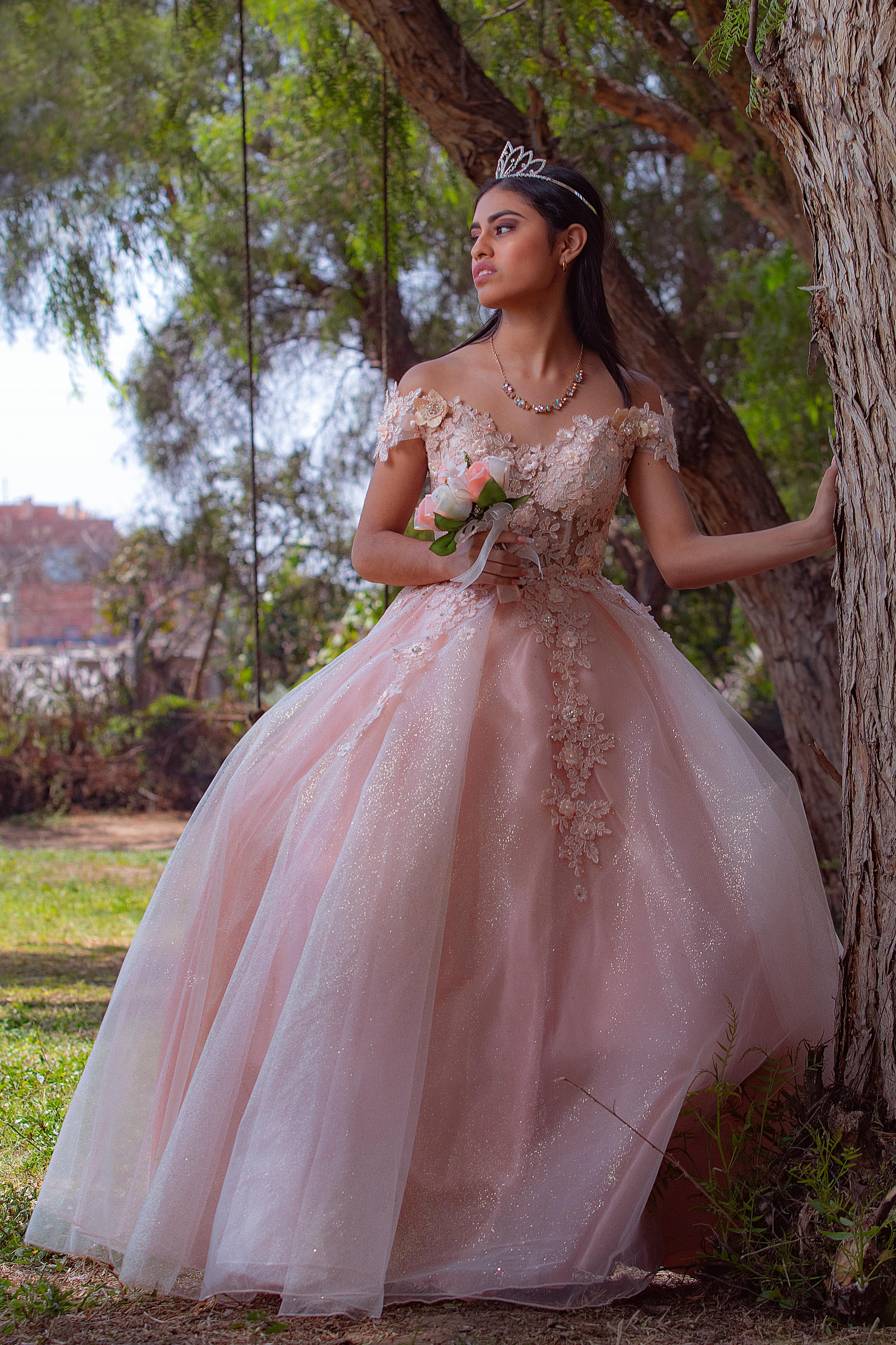 A stunning bride in a sparkling gown stands elegantly against a tree, showcasing her wedding dress and crown.