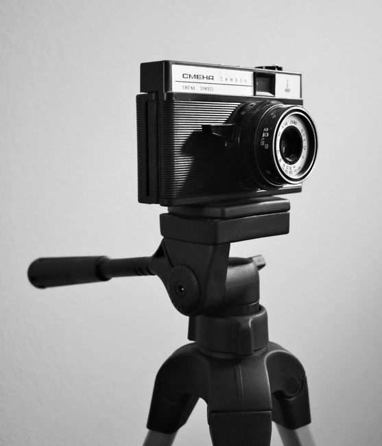 A classic vintage camera mounted on a tripod captured in a black and white setting.