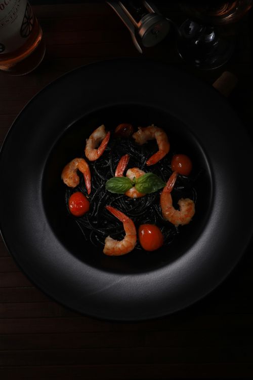Free Elegant food photography featuring shrimp and squid ink pasta on a dark plate, top view. Stock Photo