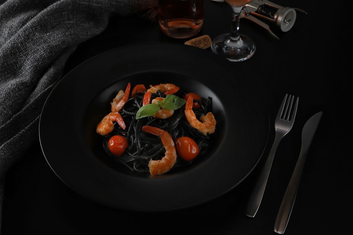 Spaghetti al nero di seppia con gamberi e pomodorini in una ciotola nera opaca, fotografia d'archivio.