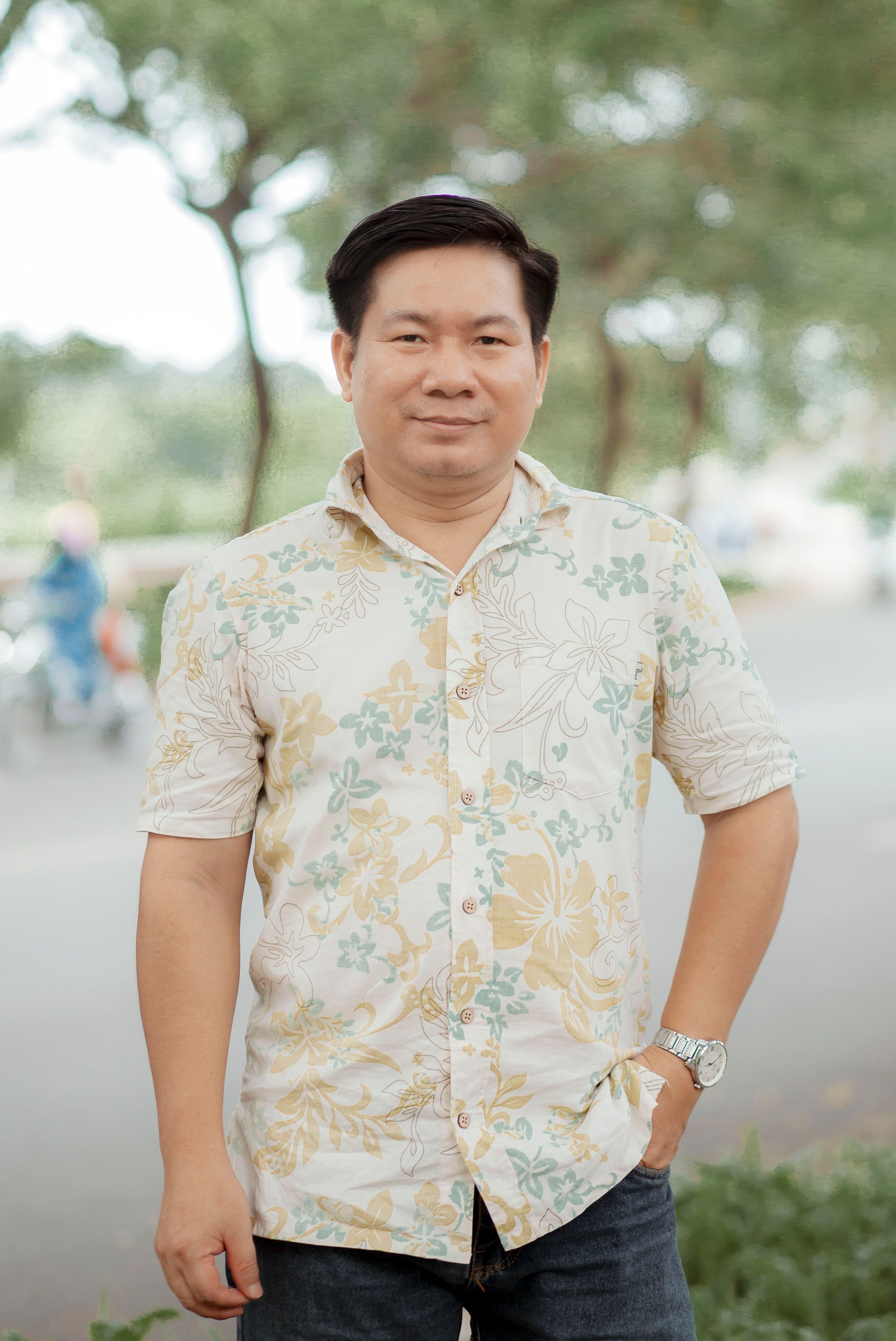A man stands confidently outdoors in a floral shirt, exuding casual style.