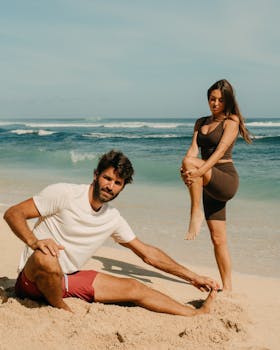 A man and woman pose on a sunny beach in activewear, embodying fitness and leisure.