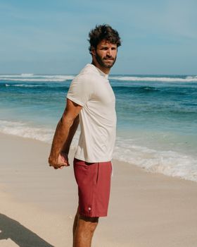 Athletic man in sportswear stretching on a sandy beach with ocean view.