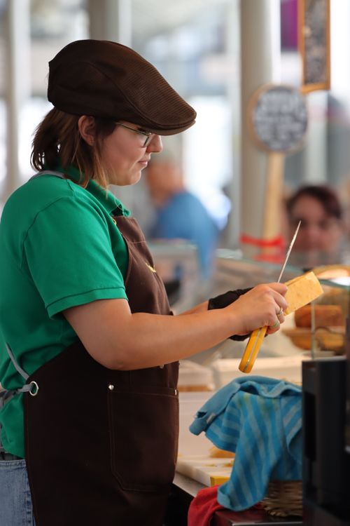Free Woman slicing cheese at a market in Porto, Portugal, showcasing local street food culture. Stock Photo
