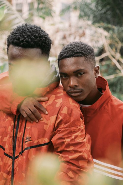 Free Candid outdoor portrait of two young men in bright jackets, embracing amid lush greenery. Stock Photo