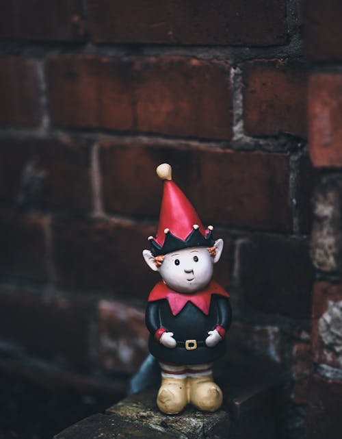 A small toy elf sitting on a brick wall