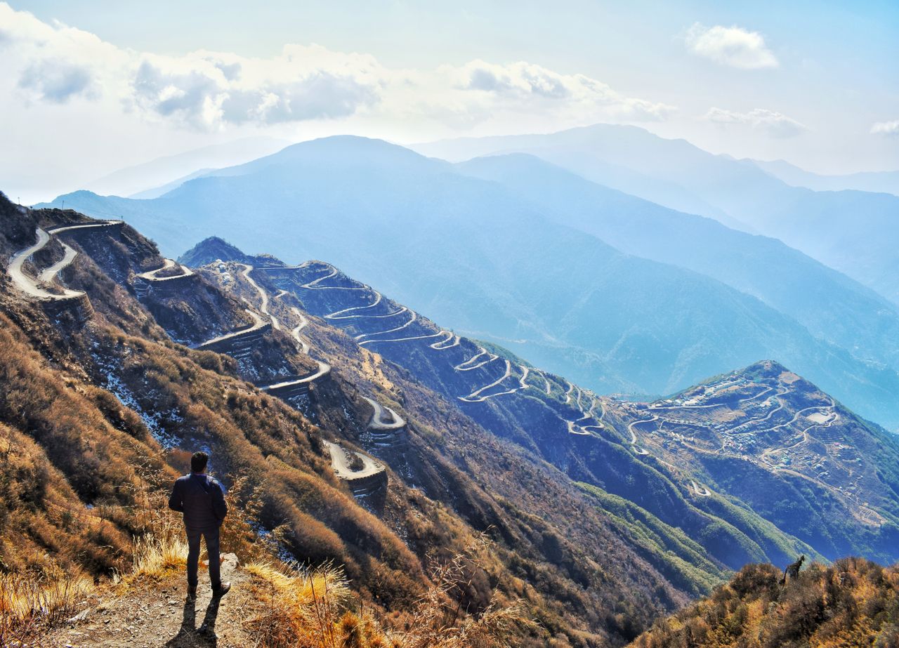a hiker overlooks a winding mountain road offering stunning panoramic