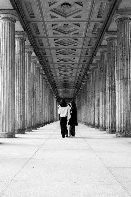 Two people walking down a long hallway with columns