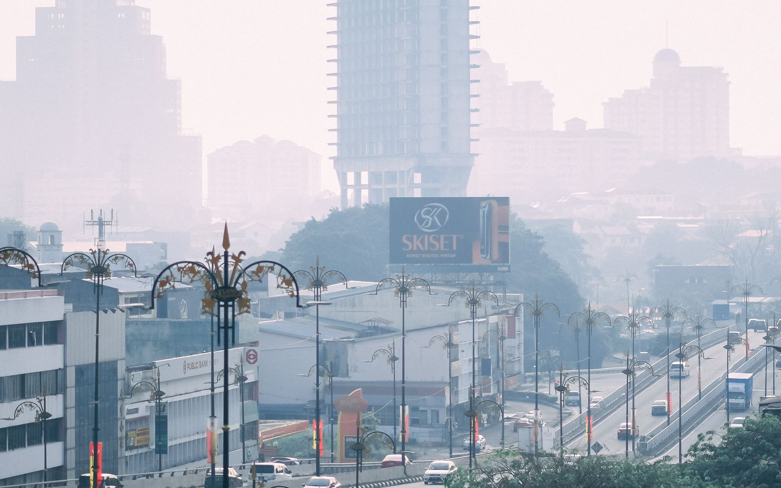 Traffic moving across an elevated overpass in Klang, Malaysia, with city buildings dimmed by haze