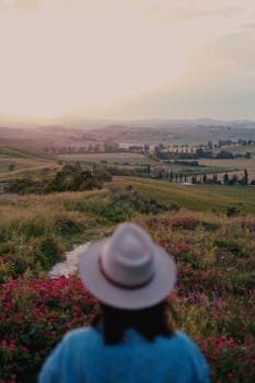 A woman in a hat enjoys a peaceful sunset over a scenic countryside landscape.