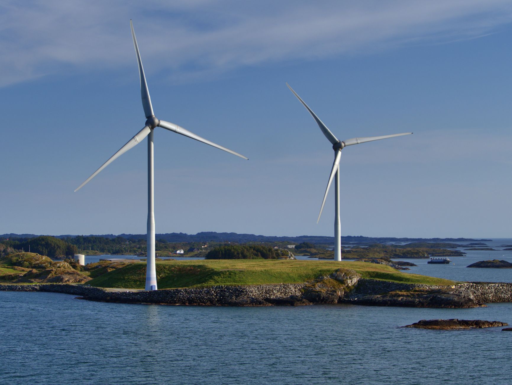 Two wind turbines on a coastal island generate renewable energy against a clear sky.