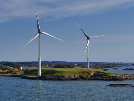 Two wind turbines on a coastal island generate renewable energy against a clear sky.