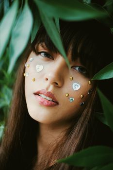 一幅女人的特写肖像，她的脸上装饰着元素，周围环绕着绿叶